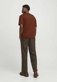 Brun bomulds t-shirt med rund hals, parret med brune bukser og brune sko, set bagfra mod en lys baggrund.