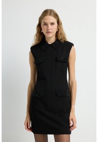 Schwarzes ärmelloses Kleid mit strukturiertem Design, verziertem Kragen und zwei Brusttaschen mit strukturierten Perlendetails.
