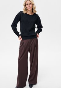 Czarny dziany sweter z diamentowym wzorem, zestawiony z szerokimi brązowymi spodniami o luźnym kroju. Strój charakteryzuje się luźnym fasonem i ściągaczami na rękawach.