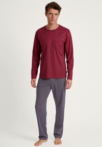 Haut bordeaux à manches longues avec une poche poitrine associé à un pantalon de pyjama à motifs dans des couleurs sombres et des designs géométriques clairs.