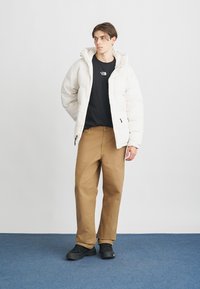 Witte pufferjas met capuchon, zwart T-shirt, beige broek en zwarte sneakers. Soepele textuur en minimalistisch ontwerp.