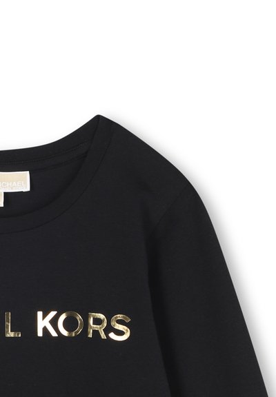 Crna pamučna majica s okruglim izrezom, s zlatnim metalnim logotipom "MICHAEL KORS" na prednjoj strani. Glatka tekstura, ležeran dizajn.
