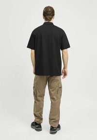 Zwarte polo met korte mouwen, relaxed fit, gecombineerd met bruine cargobroek met zijzakken en zwarte sportschoenen.