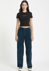 Sorte cropped t-shirt med lilla tekst, parret med turkise kordfløjspants med vid ben, der har knaplukning og klassiske lommer.