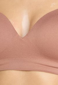 Bralette seamless mauve clair avec un décolleté en V profond, un design texturé à rayures et une large bande de soutien, sans quincaillerie visible.