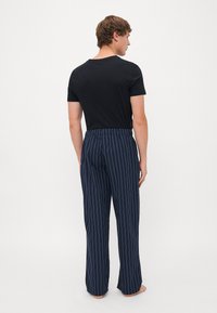 Marine gestreepte pyjamabroek met een elastische tailleband, gecombineerd met een eenvoudig zwart T-shirt met ronde hals, gezien vanuit de achterkant.
