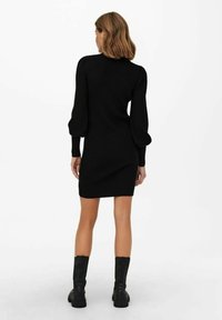 Abito a maglia nero con maniche lunghe e gonfie, dalla silhouette aderente, abbinato a stivaletti neri alla caviglia. Texture liscia.