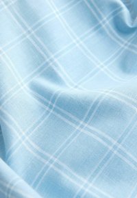 Tissu bleu clair avec un motif à carreaux blanc, présenté avec des plis doux et une texture tissée visible.