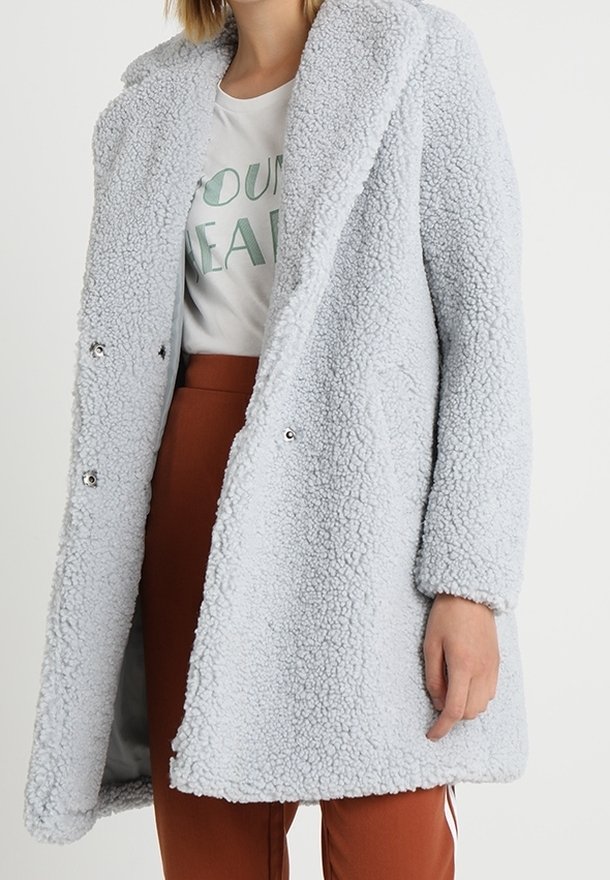 Cappotto in morbido pelliccia ecologica grigia chiara con design doppiopetto; presenta ampie rever e bottoni metallici sul davanti.