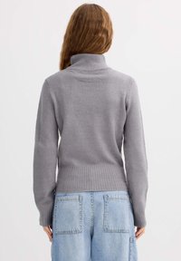 Suéter gris con cuello alto y dobladillo acanalado. Mangas largas, textura suave, silueta ajustada, usado con pantalones cargo azul claro.