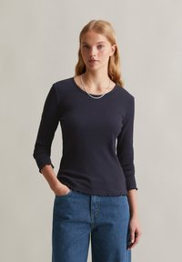 Marineblaues, gestreiftes Oberteil mit rundem Ausschnitt, Dreiviertelärmeln und gerafften Bündchen, kombiniert mit lockeren, blauen Jeans. Schlichtes Design und strukturierter Stoff.