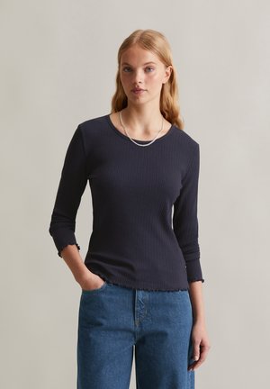Marineblauwe geribbelde top met een ronde halslijn, driekwart mouwen en gefronste manchetten, gecombineerd met losse blauwe jeans. Eenvoudig ontwerp en gestructureerde stof.