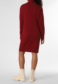 Abito maglione rosso a trecce con colletto alto, polsini e orlo a coste. Abbinato a stivali da combattimento con suola spessa di colore crema.