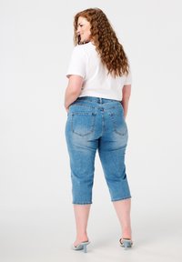 Jeans en denim bleu avec un design court, cinq poches et un léger délavage. Associés à un t-shirt blanc uni et des talons bleu clair.