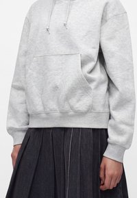 Person wearing light gray hoodie with front pocket and drawstrings paired with a dark pleated skirt, shown from chest to waist.