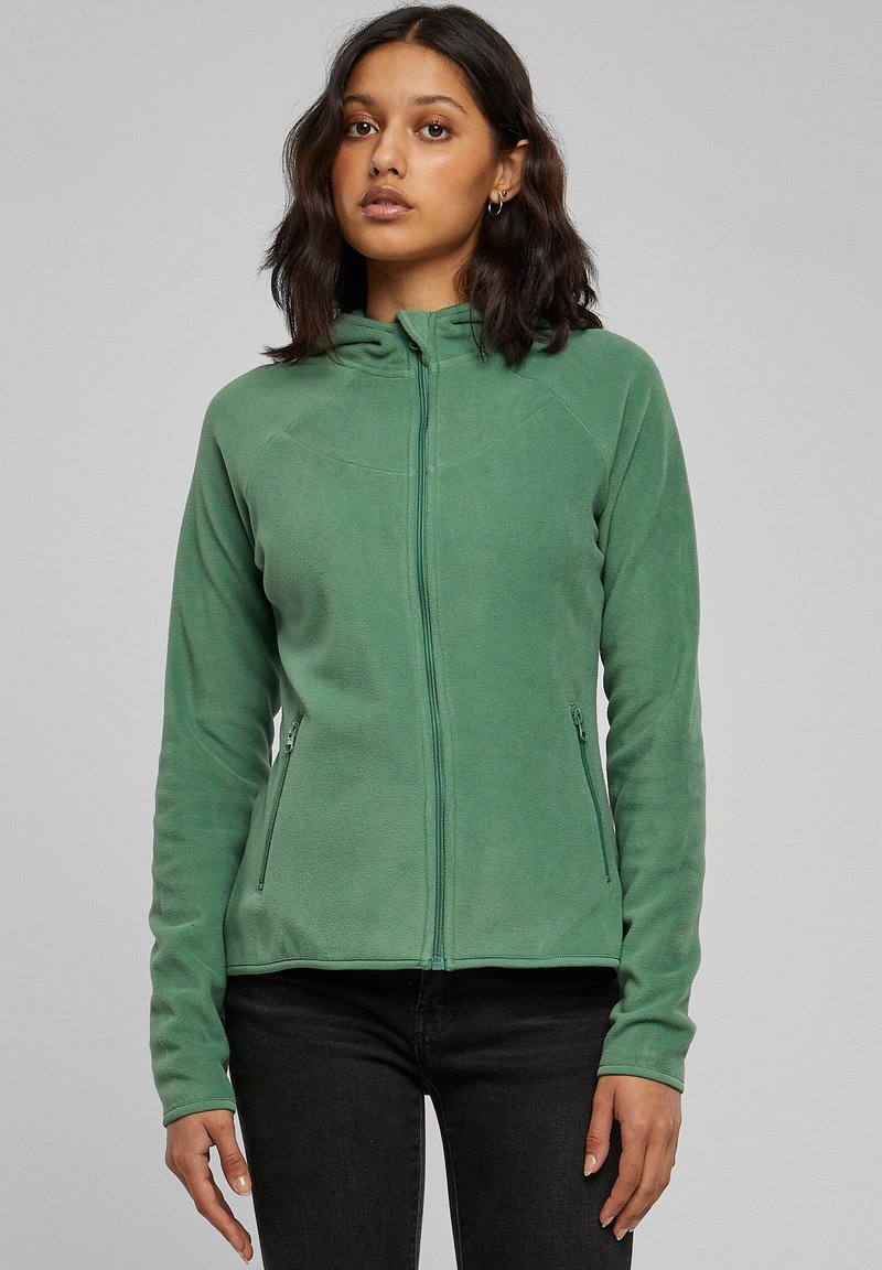 Žalia fliso striukė su užtrauktuku ir kapišonu, turinti šonines kišenes, lygų paviršių ir aptakų dizainą. Rankovės baigiasi ties riešais.