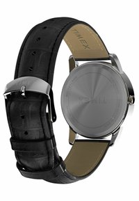 Montre en cuir noir avec un bracelet texturé, boîtier en métal argenté et fond argenté uni. Logo gravé sur la boucle.