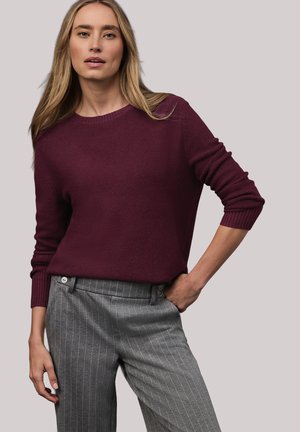 Maglione di lana color bordeaux con scollo rotondo e polsini a coste, abbinato a pantaloni grigi a righe sottili con due bottoni sulla cintura.