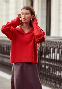Red knit sweater with a wide collar and ribbed hem, paired with a dark leather skirt. The material appears soft and textured.