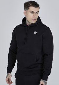 Black pullover hoodie made of cotton, featuring a front pocket and a drawstring hood, with a white logo on the left chest.