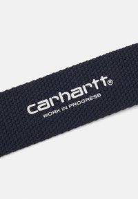 Cintura intrecciata blu navy con logo "carhartt" bianco e testo "WORK IN PROGRESS", caratterizzata da una finitura testurizzata per una migliore aderenza.