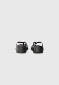 Sorte gummisandaler med lav plattform, med tynne kryssremmer og en teksturert fotbed. Designet er minimalistisk og praktisk.
