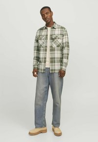 Geruite flanellen overhemd in groen en wit, met twee borstzakken, gedragen met lichtblauwe jeans en beige boots, met een relaxte pasvorm.