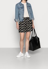 Veste en denim, pull en tricot beige, jupe à motifs noir et blanc, baskets blanches et grand sac fourre-tout noir.