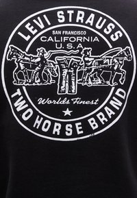 Λογότυπο της Levi Strauss με δύο άνδρες που τραβούν αντίθετα άλογα, τζιν στο κέντρο και κείμενο «San Francisco California U.S.A» σε κυκλικό σχέδιο.