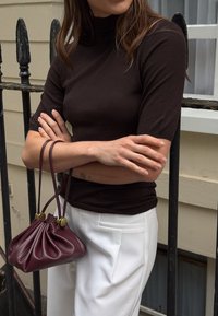 Ruskea istuva paita lyhyillä hihoilla, yhdistetty valkoisiin räätälöityihin housuihin. Pieni burgundinvärinen nahkalaukku, jossa on kerätty muotoilu ja kultaiset yksityiskohdat.