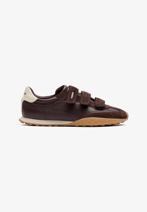 Donkerbruine sneaker met drie klittenbandsluitingen, beige hieltab en een gumrubberen zool met zeshoekig patroon.