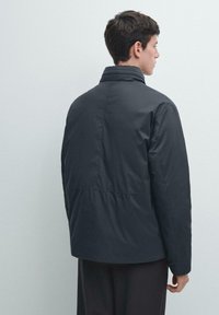 Schwarze gesteppte Jacke mit hohem Kragen, die eine glatte Textur und eine Rückennaht aufweist. Entworfen mit einer lockeren Passform und einem längeren Rückensaum.