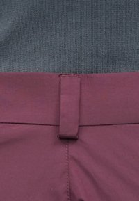 Pogled od blizu na pas maroon hlača s petljom iz tkanine i sivim pletenim vrhom uvučenim unutra.