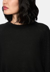 Schwarzer gestrickter Pullover mit rundem Ausschnitt und weicher Textur, von der Schulter aufwärts aufgenommen, mit einer lässigen Passform.