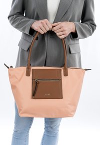 Borsa tote in nylon rosa con dettagli in pelle marrone, dotata di una tasca frontale con cerniera e manici curvi. Il design è spazioso e funzionale.
