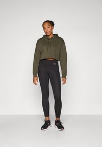Hoodie cropped verde-azeitona, leggings pretas e sapatilhas pretas com detalhes em rosa. Texturas suaves e detalhe com cordão no hoodie.