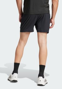 Schwarze Sportshorts mit einem elastischen Bund, aus leichtem Material und in entspannter Passform; kombiniert mit weißen Turnschuhen und schwarzen Kniestrümpfen.