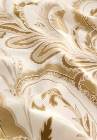 Tissu crème avec un motif paisley doré, présentant des tourbillons complexes et des accents floraux, texture lisse et éclat subtil.
