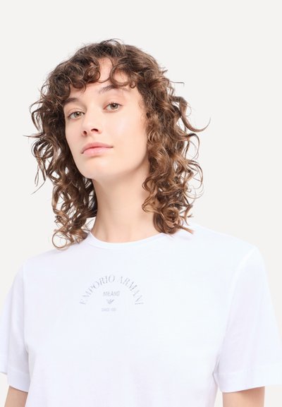 Witte katoenen t-shirt met korte mouwen, met een geborduurd logo in het grijs op de borst, ronde halslijn, gladde textuur.