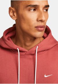 Röd hoodie i bomullsblandning, med en främre ficka, vita snören och en liten vit Nike-logotyp på bröstet.