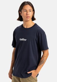 Camiseta de algodón azul marino con mangas cortas, escote redondo y logo blanco de Quiksilver en el pecho. Ajuste cómodo y casual.