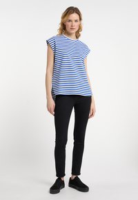 Blå og hvid stribet ærmeløs top med en rund halsudskæring, parret med sorte skinny jeans og sorte sneakers på en neutral baggrund.