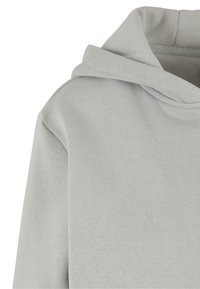Lys grå hettegenser med myk, teksturert stoff, avslappet passform og snorhette. Sømdetaljer fremhever designet.
