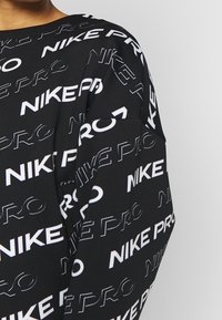 Top sportivo nero con testo ripetuto "NIKE PRO" bianco in diverse dimensioni, realizzato in tessuto morbido ed elastico con una vestibilità comoda.