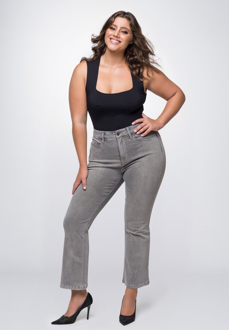 Zwarte body met een vierkante halslijn, gecombineerd met hooggerande grijze jeans. Model draagt zwarte puntige hakken; haar is in losse golven.