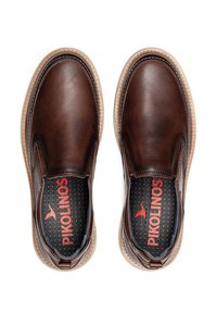 Zapatos de cuero marrón sin cordones con una textura suave, suela beige y un logo rojo en la plantilla negra acolchada, con bordes de diseño estilizado.