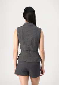 Top peplum senza maniche grigio e nero con motivo a quadretti e vita con cintura, abbinato a pantaloni corti grigio scuro, visto da dietro.
