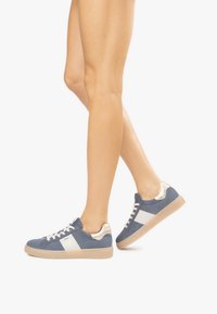 Baskets en daim bleu avec une rayure blanche, des accents beiges, une surface texturée et une semelle en gomme, dotées de lacets et d'un col rembourré.