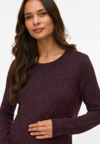 Pull bordeaux en tricot doux avec des manches longues et un col rond. La texture semble moelleuse, avec des poignets ajustés.