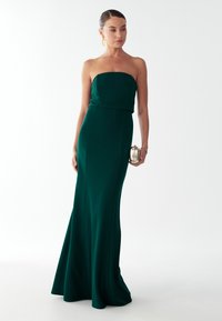 Zielona sukienka bez ramiączek z dopasowanym gorsetem i rozkloszowaną spódnicą. Gładki materiał o matowym wykończeniu. Dopełniona metaliczną kopertówką.